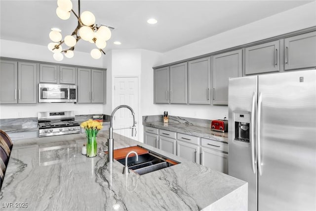 kitchen featuring light stone countertops, gray cabinets, a sink, appliances with stainless steel finishes, and a chandelier