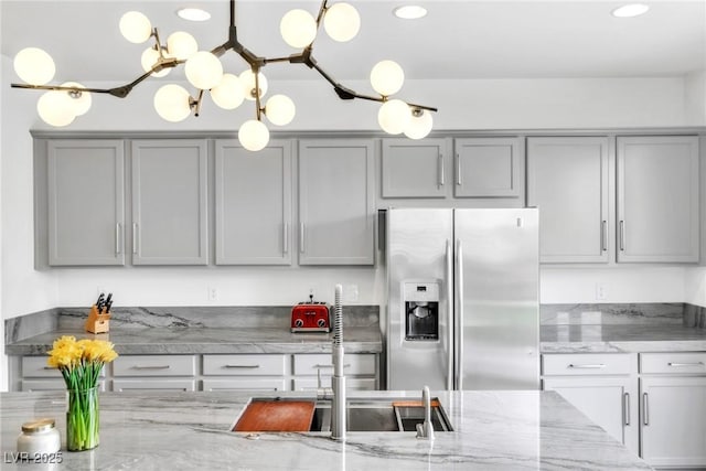 kitchen featuring gray cabinets, light stone countertops, stainless steel fridge, and pendant lighting