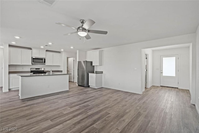 kitchen with appliances with stainless steel finishes, a ceiling fan, open floor plan, white cabinets, and wood finished floors