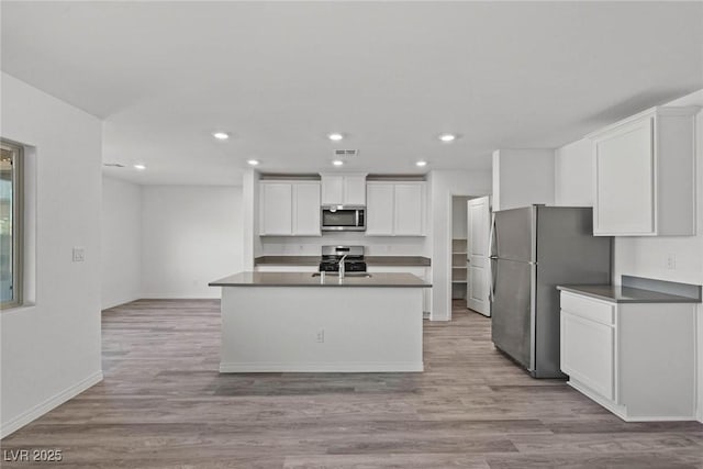 kitchen featuring white cabinets, dark countertops, appliances with stainless steel finishes, light wood-type flooring, and a sink