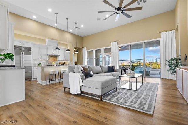 living room featuring wood finished floors, visible vents, a high ceiling, recessed lighting, and ceiling fan