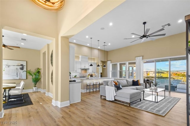 living area featuring light wood-type flooring, visible vents, a towering ceiling, baseboards, and ceiling fan