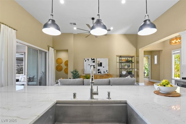 kitchen featuring open floor plan, light stone counters, visible vents, and pendant lighting