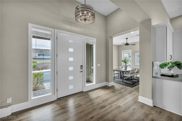 entrance foyer with ceiling fan with notable chandelier, baseboards, and wood finished floors