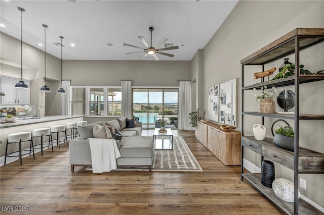 living area with a ceiling fan, wood finished floors, visible vents, and a towering ceiling