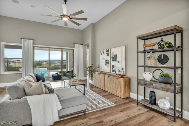 living area featuring a towering ceiling, ceiling fan, baseboards, and wood finished floors