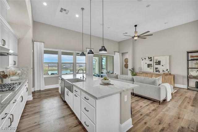 kitchen featuring visible vents, a center island with sink, a sink, light wood-style floors, and stainless steel gas stovetop