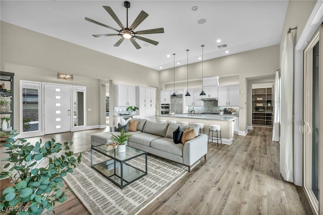 living room with light wood finished floors, visible vents, ceiling fan, baseboards, and a towering ceiling