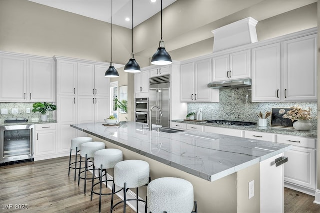 kitchen featuring a sink, wine cooler, appliances with stainless steel finishes, under cabinet range hood, and white cabinetry