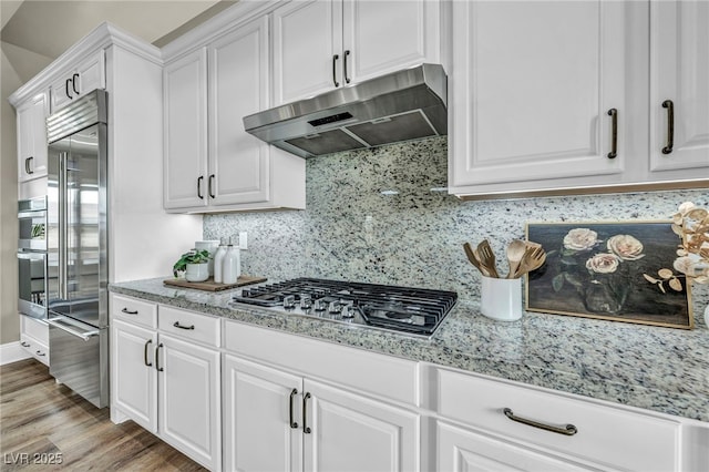 kitchen featuring light wood-style flooring, under cabinet range hood, backsplash, white cabinetry, and stainless steel appliances