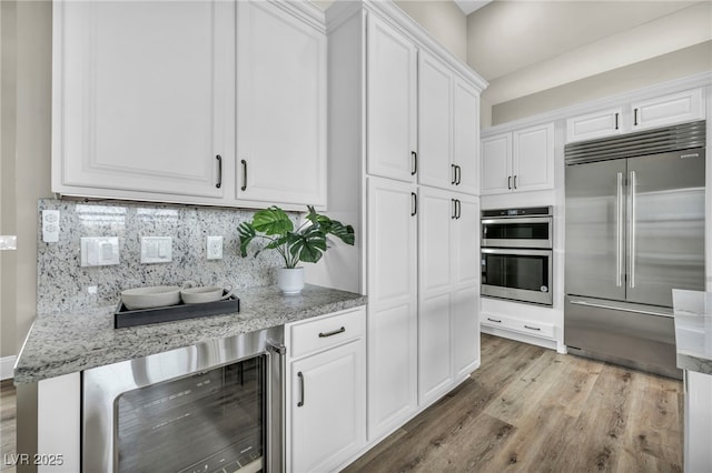 kitchen with tasteful backsplash, light stone countertops, light wood-type flooring, appliances with stainless steel finishes, and white cabinets