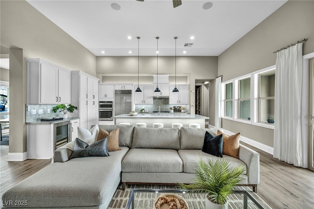 living area with visible vents, baseboards, recessed lighting, light wood-style floors, and a towering ceiling