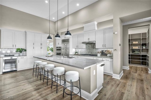 kitchen with a sink, wine cooler, white cabinets, under cabinet range hood, and appliances with stainless steel finishes