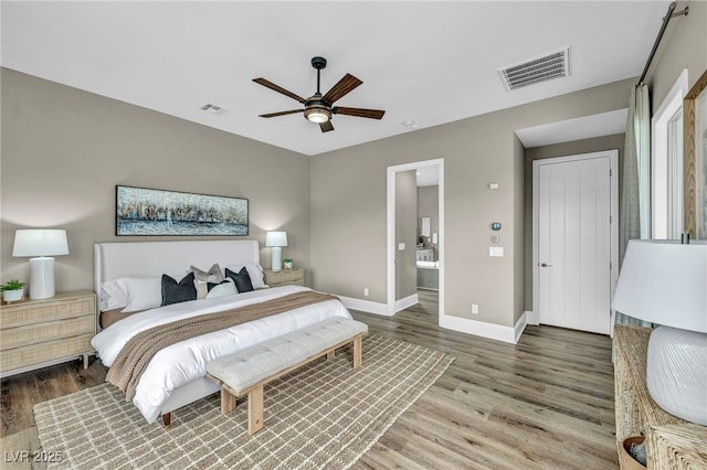 bedroom featuring connected bathroom, visible vents, baseboards, and wood finished floors