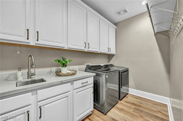 clothes washing area featuring visible vents, washer and clothes dryer, light wood-style flooring, cabinet space, and a sink