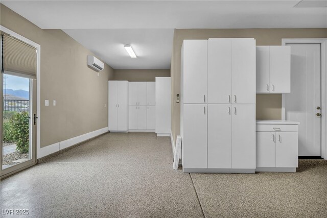 interior space with baseboards, light speckled floor, an AC wall unit, and access to exterior