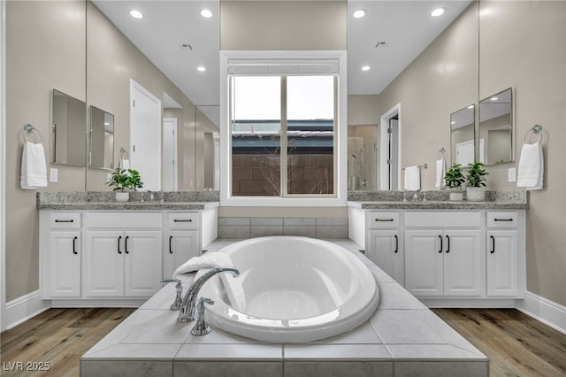 bathroom with baseboards, two vanities, a garden tub, and wood finished floors