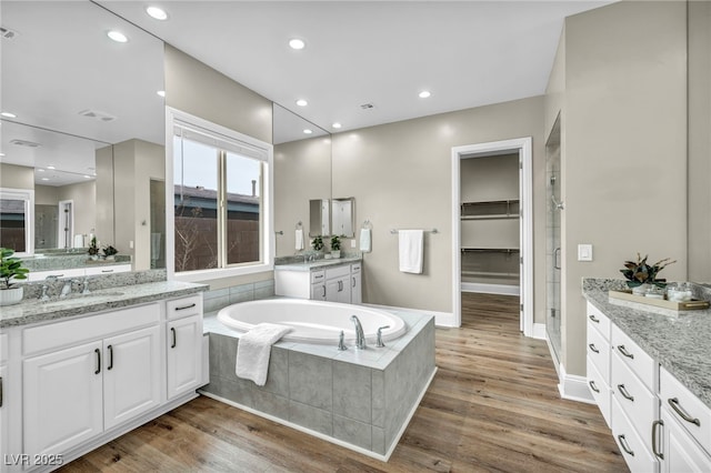 full bath with two vanities, a sink, wood finished floors, recessed lighting, and a bath