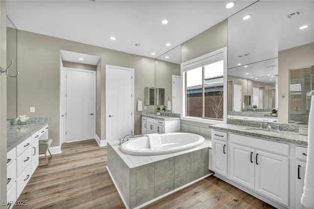 full bath with a sink, visible vents, wood finished floors, and a bath