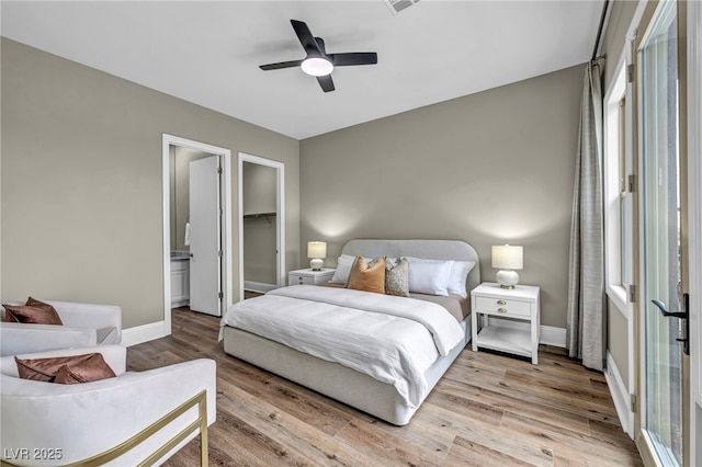 bedroom with a walk in closet, wood finished floors, baseboards, and a ceiling fan