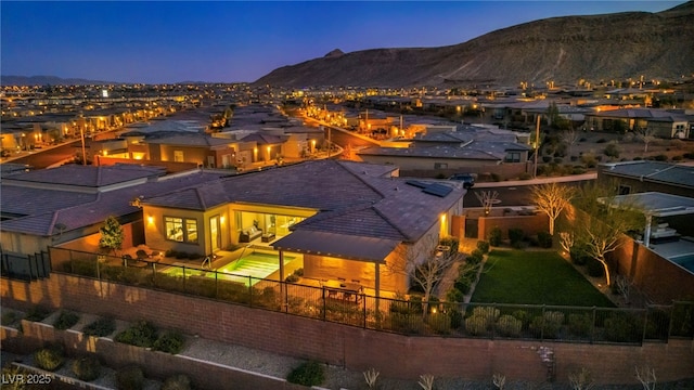 back of house at dusk with a mountain view, a lawn, and a fenced backyard