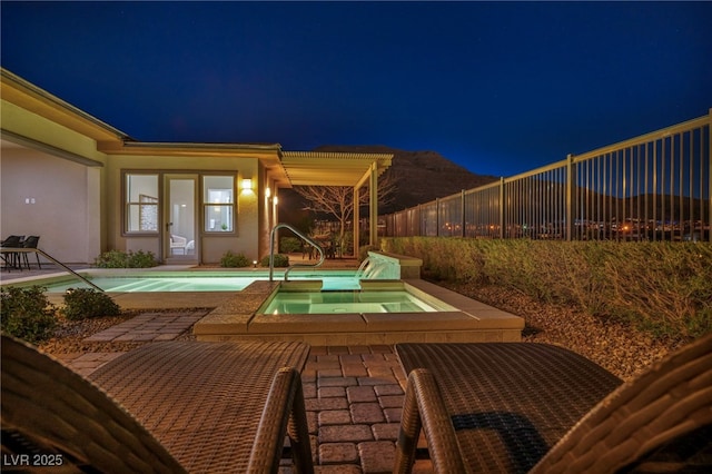 pool at night featuring a fenced in pool, fence, a patio area, an in ground hot tub, and a sink