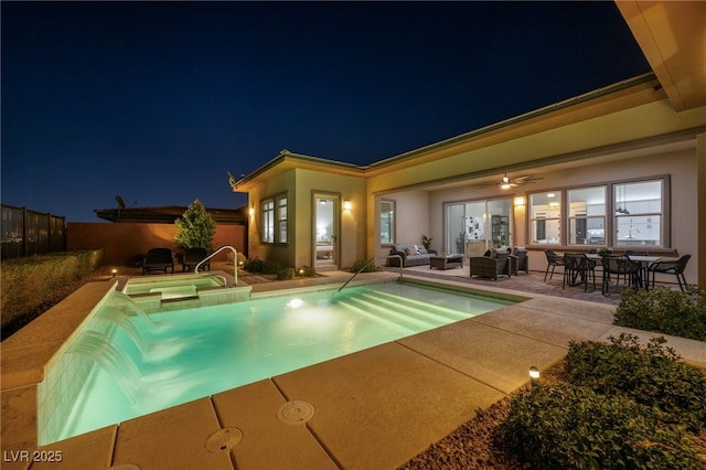 pool at night featuring a patio area, fence, and a pool with connected hot tub