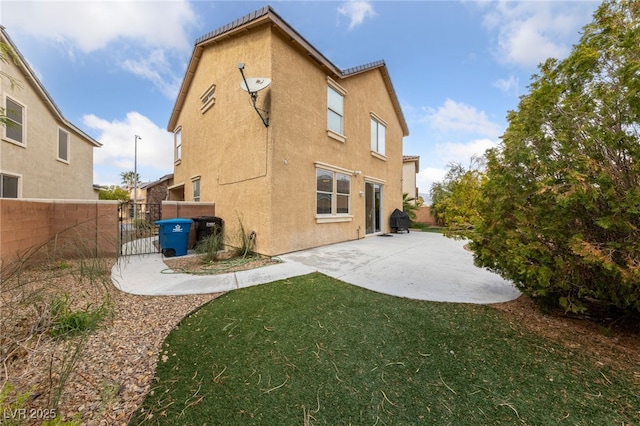 back of property featuring a lawn, a gate, fence, a patio area, and stucco siding