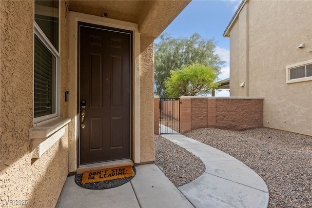 entrance to property featuring a gate, fence, and stucco siding