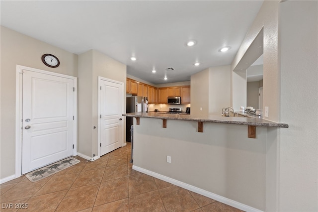 kitchen with light tile patterned floors, stone countertops, stainless steel appliances, visible vents, and a kitchen bar