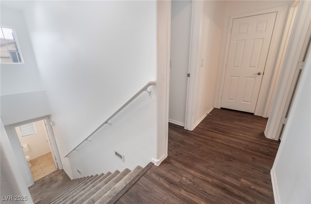 hallway with baseboards, visible vents, dark wood finished floors, and an upstairs landing