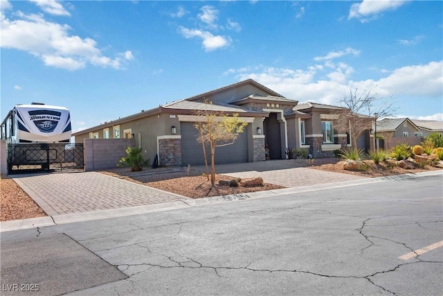 prairie-style house with driveway, stone siding, an attached garage, fence, and stucco siding