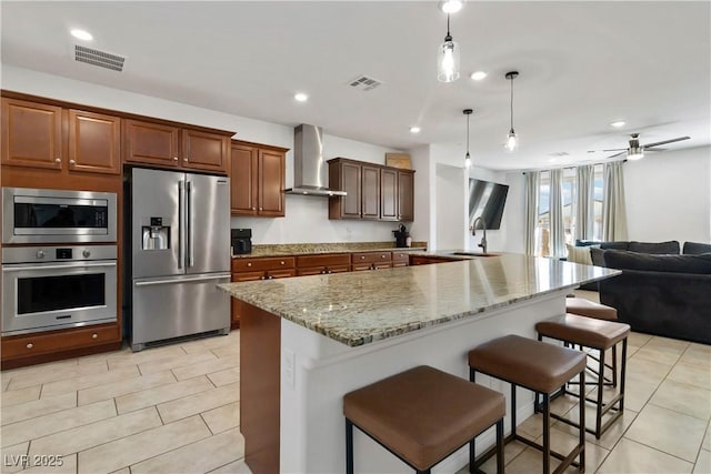 kitchen with wall chimney exhaust hood, visible vents, stainless steel appliances, and open floor plan