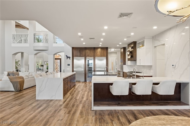 kitchen featuring visible vents, an island with sink, a peninsula, light wood-style floors, and a sink