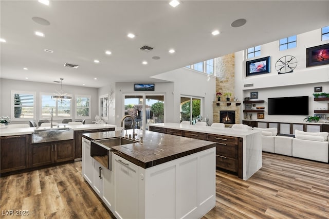 kitchen featuring a stone fireplace, an island with sink, a sink, and visible vents