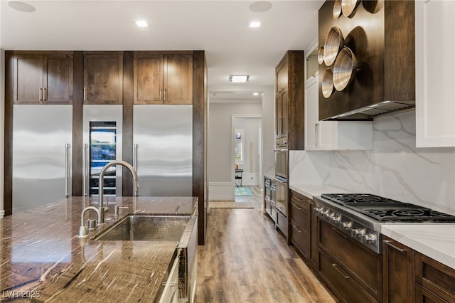 kitchen with light stone counters, stainless steel appliances, decorative backsplash, a sink, and wall chimney exhaust hood