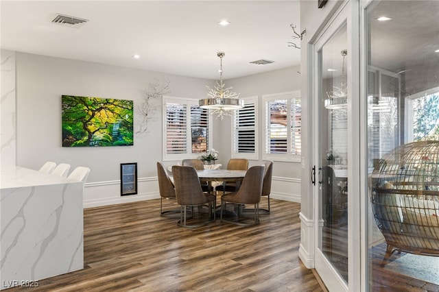 dining area featuring dark wood-style flooring, visible vents, and an inviting chandelier