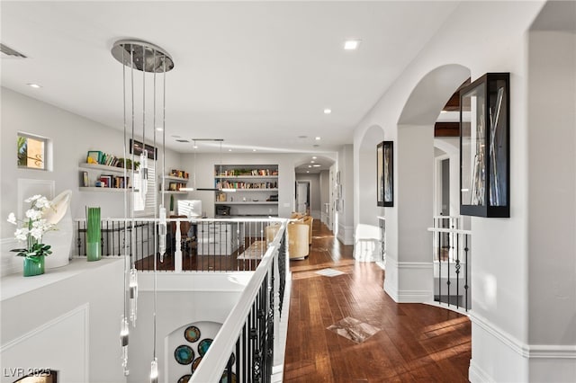 hallway featuring arched walkways, dark wood-style flooring, recessed lighting, visible vents, and baseboards