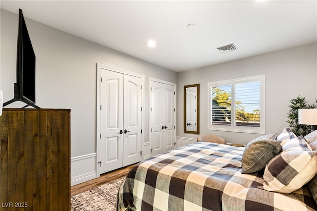 bedroom featuring visible vents, two closets, and wood finished floors