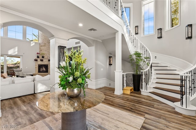 living room with a lit fireplace, a high ceiling, visible vents, and wood finished floors