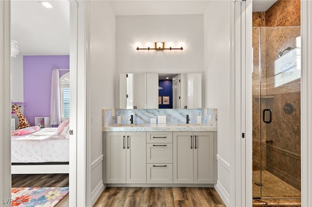 ensuite bathroom featuring double vanity, a stall shower, decorative backsplash, connected bathroom, and wood finished floors