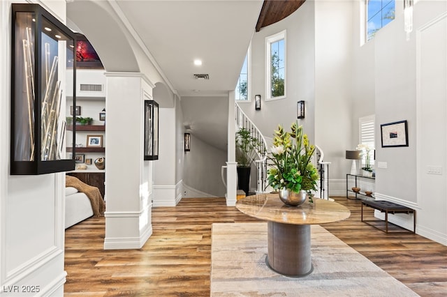 hallway featuring light wood-style floors, decorative columns, visible vents, and stairway