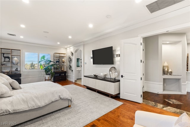 bedroom with visible vents, arched walkways, wood finished floors, and ornamental molding