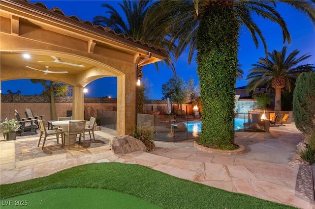 patio at night with outdoor dining space, a fenced backyard, and a fenced in pool