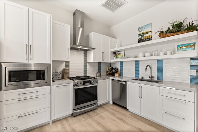 kitchen with a sink, visible vents, white cabinetry, wall chimney range hood, and appliances with stainless steel finishes