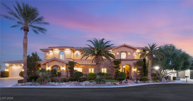 mediterranean / spanish house with an attached garage, a tiled roof, concrete driveway, and stucco siding