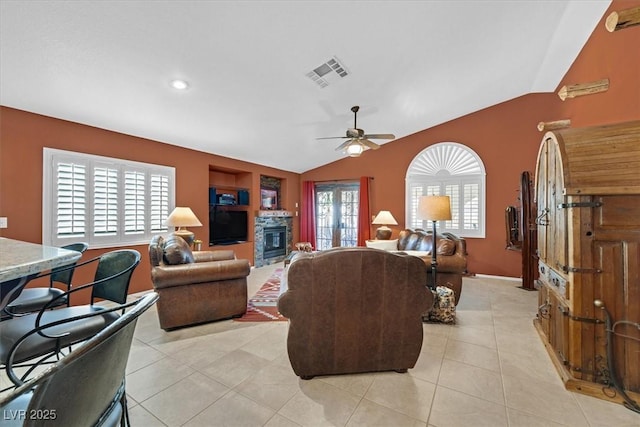 living room featuring light tile patterned floors, lofted ceiling, visible vents, a ceiling fan, and a glass covered fireplace