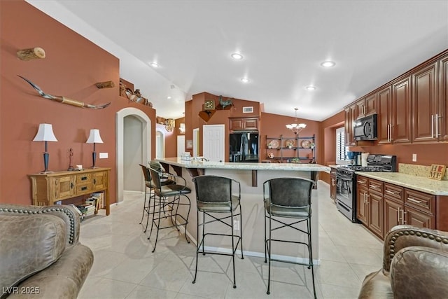 kitchen featuring arched walkways, an inviting chandelier, vaulted ceiling, black appliances, and a kitchen bar