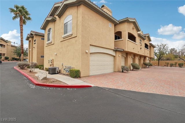 exterior space with stucco siding, decorative driveway, a garage, and a chimney