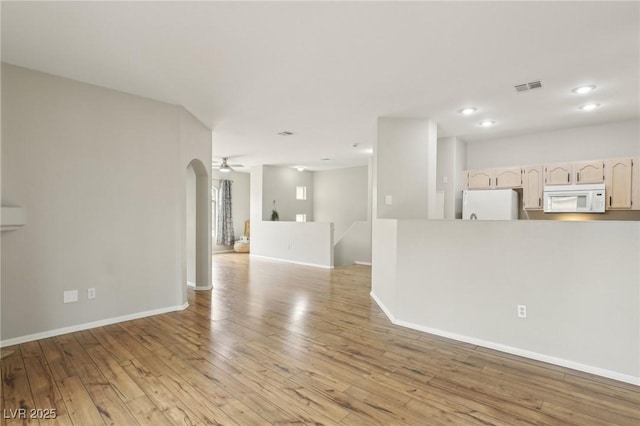 unfurnished living room featuring visible vents, arched walkways, light wood-style floors, and baseboards